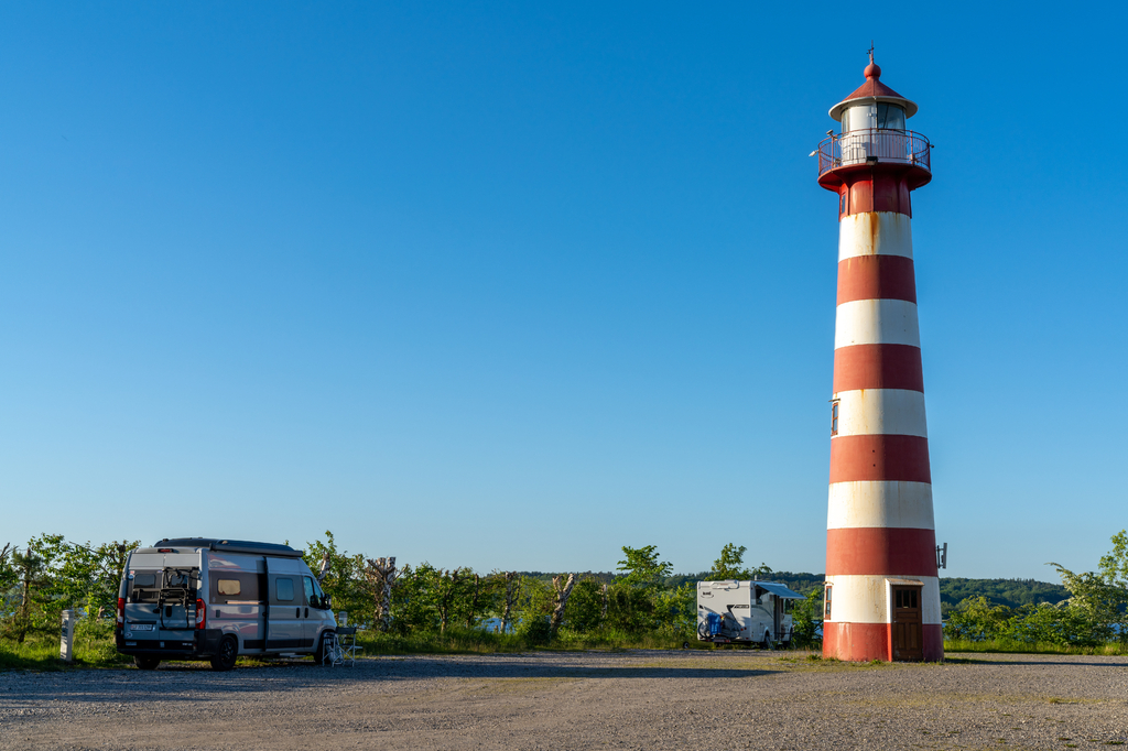 Lais Puzzle - graues Wohnmobil neben einem rot-weißen Leuchtturm an der dänischen Küste unter wolkenlosem blauem Himmel geparkt - 2.000 Teile p-275212