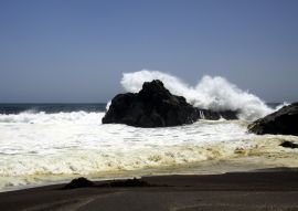 Lais Puzzle - Kraftvolle Wellen, die auf einem Felsen zusammenstoßen und Wasser in der Luft am entfernten schwarzen Lavasandstrand an der Pazifikküste spritzen - Cobquecura Piedra De La Loberia, Chile - 100, 200, 500 & 1.000 Teile