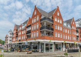 Lais Puzzle - Groesbeek, Die Niederlande - Menschen genießen ein Getränk und Essen vor einem modernen Gebäude mit Restaurant und Geschäften - 100, 200, 500 & 1.000 Teile