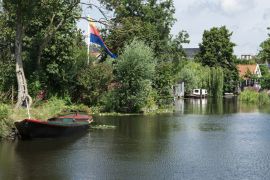 Lais Puzzle - Ruderboot im Fluss, mit Häusern, Bäumen und Brücke. Broek op Langedijk, Niederlande - 2.000 Teile