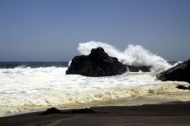 Lais Puzzle - Kraftvolle Wellen, die auf einem Felsen zusammenstoßen und Wasser in der Luft am entfernten schwarzen Lavasandstrand an der Pazifikküste spritzen - Cobquecura Piedra De La Loberia, Chile - 2.000 Teile