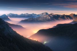 Lais Puzzle - Berge im Nebel bei schöner Herbstnacht in den Dolomiten, Italien. Landschaft mit alpinem Bergtal, niedrigen Wolken, Wald, buntem Himmel mit Sternen, Stadtbeleuchtung in der Abenddämmerung. Luftaufnahme. Passo Giau - 2.000 Teile