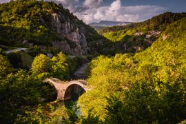 Lais Puzzle - Plakidas-Brücke mit dem Dorf Kipi im Hintergrund. Gewölbte Steinbrücke von Kalogeriko über den Fluss Voidomatis. Zentrale Zagoria, Epirus, Griechenland - 2.000 Teile
