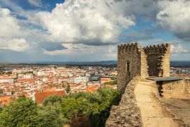 Lais Puzzle - Schlossturm von Castelo Branco, Portugal, mit der Stadt im Hintergrund und einem Himmel mit großen Wolken - 2.000 Teile
