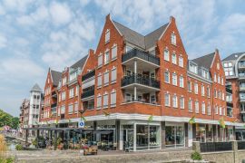 Lais Puzzle - Groesbeek, Die Niederlande - Menschen genießen ein Getränk und Essen vor einem modernen Gebäude mit Restaurant und Geschäften - 2.000 Teile