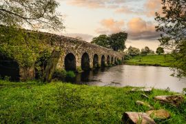 Lais Puzzle - Alte Steinbogenbrücke aus dem 12. Jahrhundert über einen Fluss, Felsen auf der ersten Ebene. Grüne Felder und Bäume. Dramatischer Himmel bei Sonnenuntergang. Grafschaft Meath, Irland - 2.000 Teile