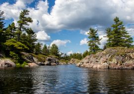 Lais Puzzle - Felsen, Bäume, blauer Himmel, weiße Wolken und Wasser an einem Sommertag am Bad River in Ontario, Kanada - 1.000 Teile