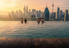 Lais Puzzle - Reisende mit Blick auf die Skyline von Kuala Lumpur im Swimmingpool auf dem Dach eines Hotels bei Sonnenaufgang in Kuala Lumpur, Malaysia - 1.000 Teile