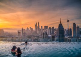 Lais Puzzle - Reisende mit Blick auf die Skyline von Kuala Lumpur im Swimmingpool auf dem Dach eines Hotels bei Sonnenaufgang in Kuala Lumpur, Malaysia - 1.000 Teile