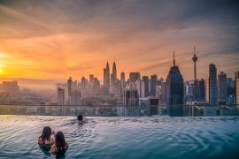 Lais Puzzle - Reisende mit Blick auf die Skyline von Kuala Lumpur im Swimmingpool auf dem Dach eines Hotels bei Sonnenaufgang in Kuala Lumpur, Malaysia - 2.000 Teile