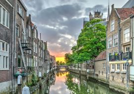 Lais Puzzle - Eine Gracht im alten mittelalterlichen Stadtzentrum von Dordrecht, Niederlande, mit Häusern auf beiden Seiten und einem orangeroten Sonnenuntergang in der Ferne - 1.000 Teile
