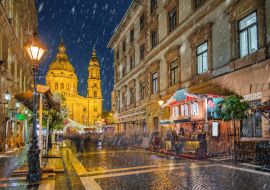 Lais Puzzle - Budapest, Ungarn - Verschneite Nacht auf einem Weihnachtsmarkt und einer Einkaufsstraße mit Straßenlaternen, festlicher Dekoration und der St.-Stephans-Basilika im Hintergrund - 1.000 Teile