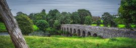 Lais Puzzle - Alte Bective Bridge aus dem 12. Jahrhundert mit Steinbogen über den Fluss Boyne mit großem Baumstamm, umgeben von grünen Feldern und Wäldern, Grafschaft Meath, Irland, Panorama - 1.000 Teile