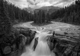 Lais Puzzle - Frau steht am Rande einer Klippe an einem wunderschönen Wasserfall in den kanadischen Rockies während eines Sommertages. Aufgenommen in Sunwapta Falls, Jasper, Alberta, Kanada in schwarz weiß - 1.000 Teile
