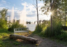 Lais Puzzle - Stadtpark Ainolan puisto in Oulu, Finnland. Springbrunnen in der Sonne und Wohnhäuser im Hintergrund - 1.000 Teile