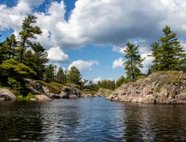 Lais Puzzle - Felsen, Bäume, blauer Himmel, weiße Wolken und Wasser an einem Sommertag am Bad River in Ontario, Kanada - 1.000 Teile